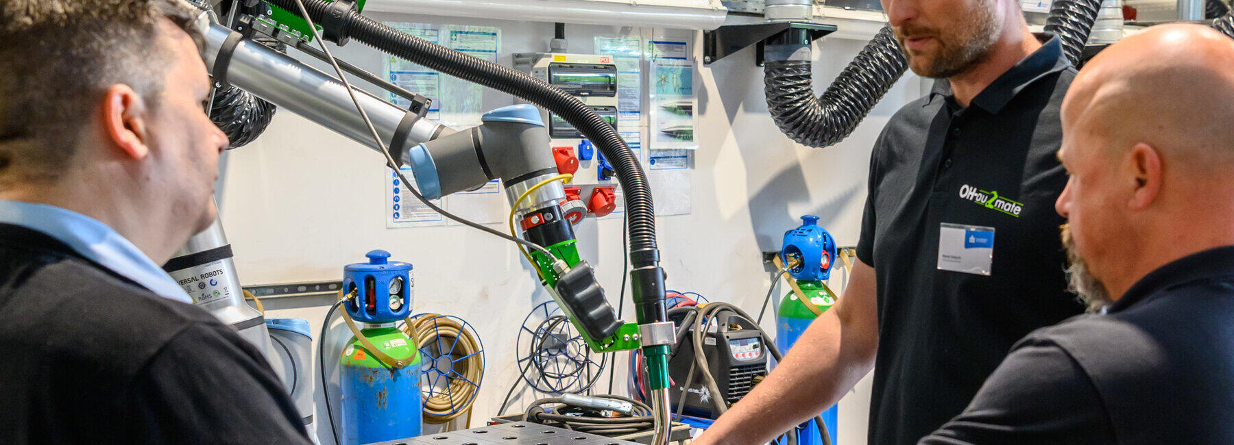 Drei männliche personen stehen an einem Schweißroboter
