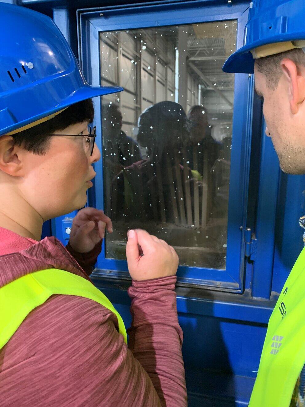 Zwei personen schauen durch ein Fenster in eine Anlage