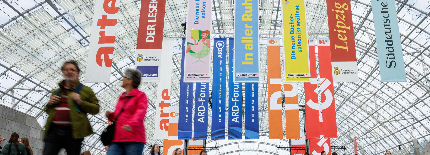 Blick in messehalle mit Menschen und bunten Bannern