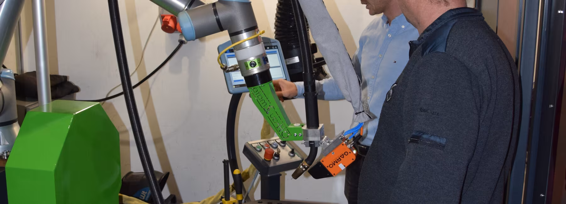 Two men are standing next to a welding robot