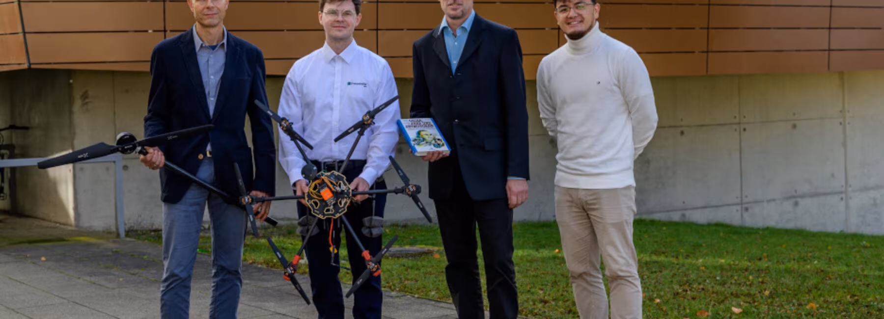 Four men with a drone are standing in front of a building