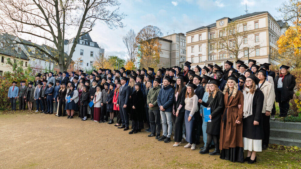 Absolvent:innen haben sich für das Gruppenfoto auf dem Platz unterhalb des Hauptgebäudes aufgestellt.