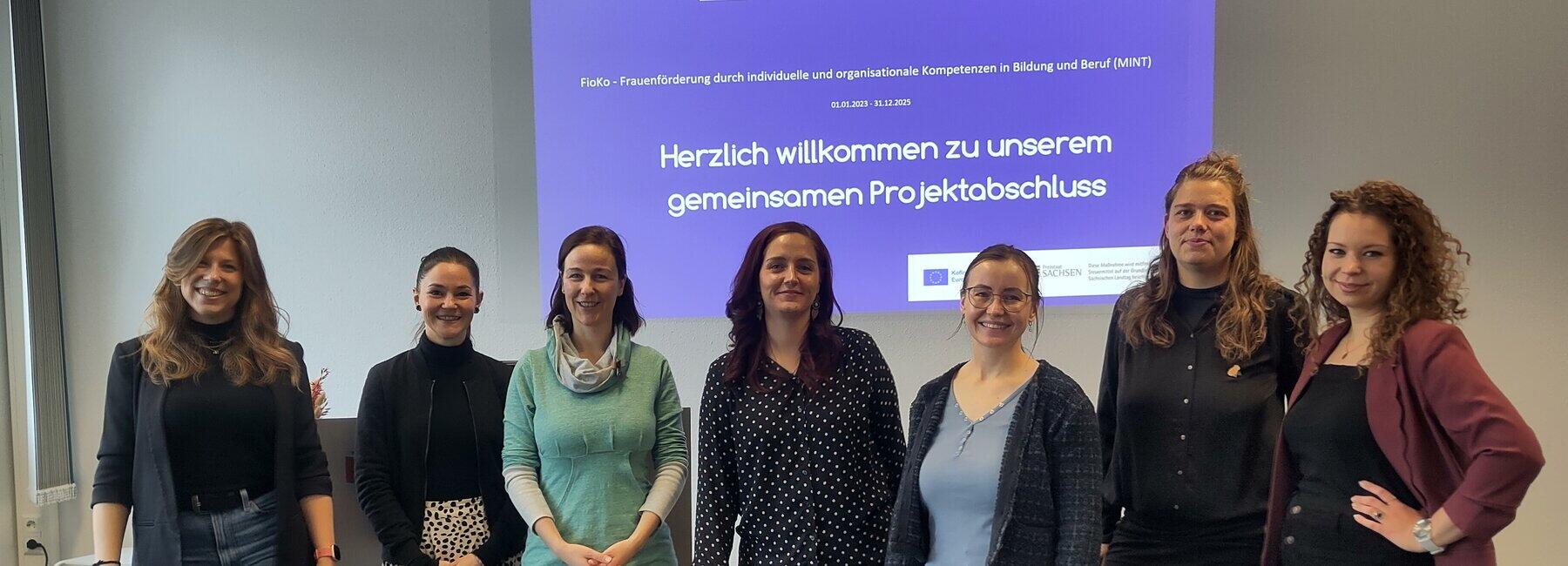 Sieben weibliche Personen stehen vor einer Präsentationswand