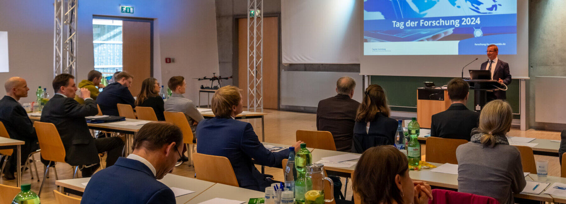 Blick aus dem Zuschauerraum ehruas auf eine männliche Person vor einer Projektionswand