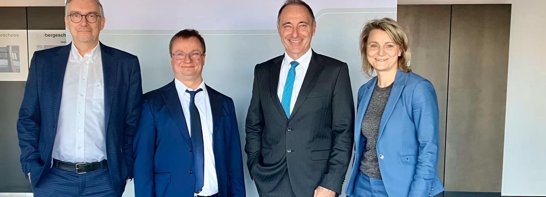 Three men and one woman, all wearing suits, are standing in front of a roll-up banner on which the words ‘State Office for Taxation and Finance’ and ‘Free State of Saxony’ can be seen between the Saxon coat of arms.