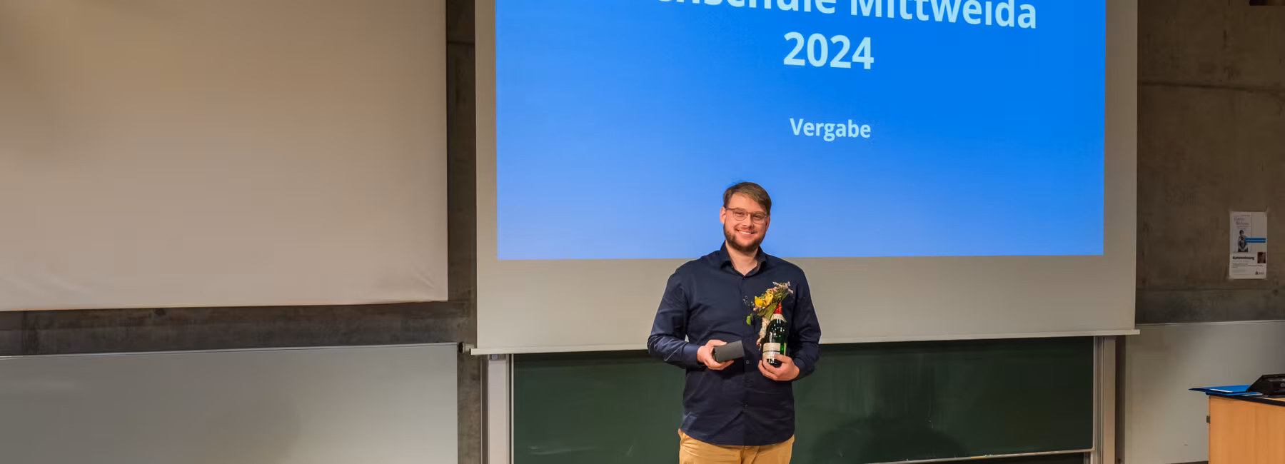 A man is standing in front of a projection screen holding a prize