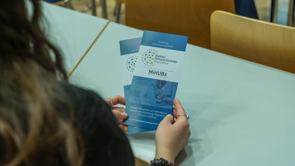 Eine Person, von hinten im Anschnitt zu sehen, hält den MiHUBx-Flyer in den Händen.