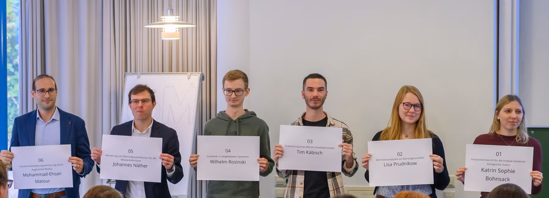 Sechs Personen halten je ein großes Namensschild hoch vor Publikum