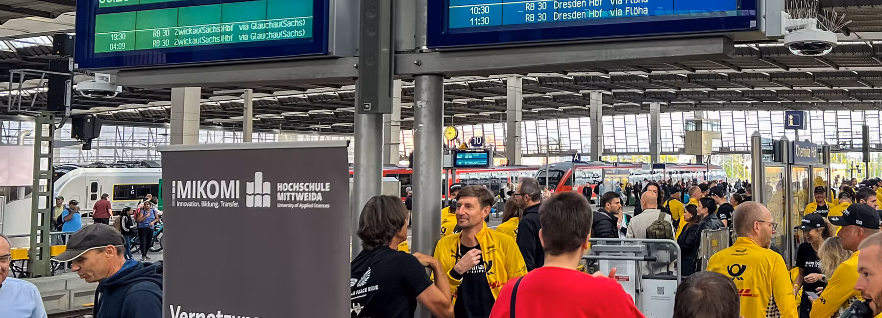 Menschen, darunter viele Sportler im gelben DHL-Trikot an einem Bahnsteig.