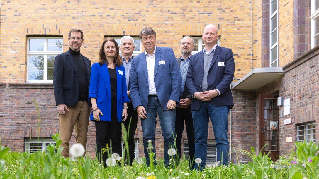 eine personengruppe steht in einer Blumenwiese vor einer Gebäudewand