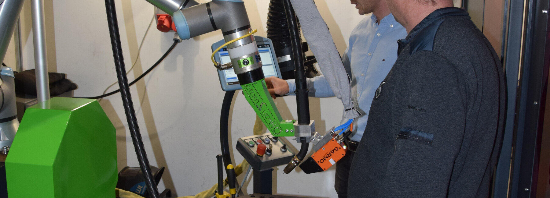 Zwei männliche Personen stehen an einem Schweißroboter