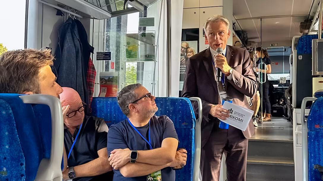Eine männliche Person mit Mikrofon in der Hand steht in einem Zug und spricht.