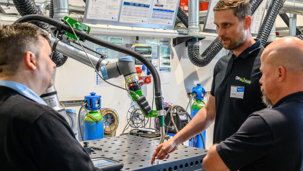 Drei männliche personen stehen an einem Schweißroboter