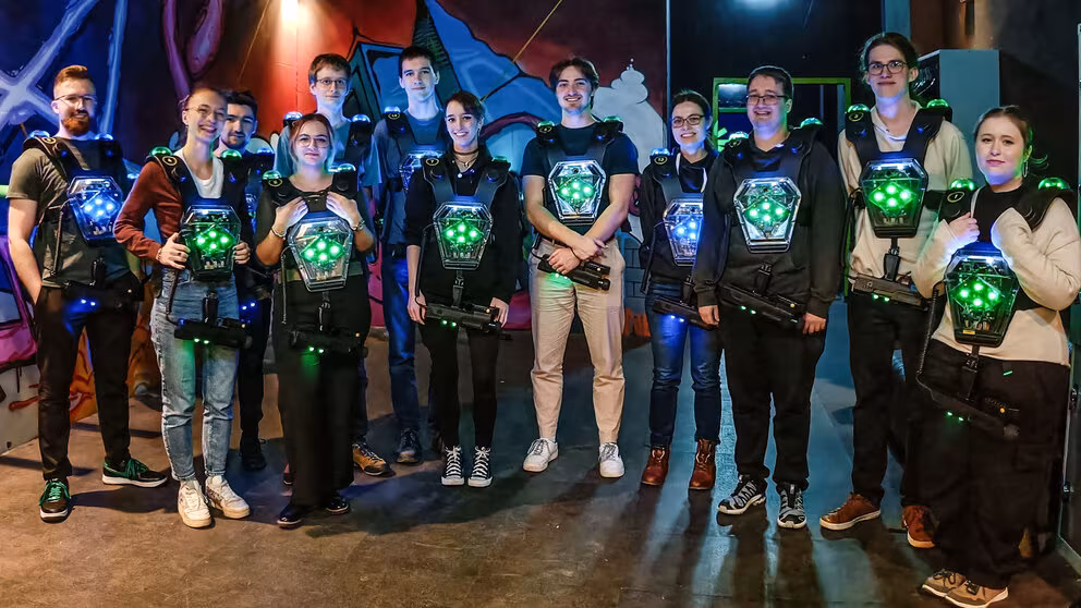 Eine Gruppe von 13 fröhlichen jungen Menschen mit Laser-Tag-Westen und -Phaser