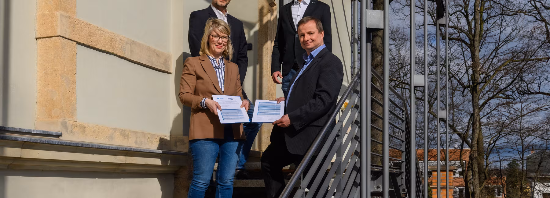 Vier Personen auf einer Treppe mit dem Jahresarbeitspapier in den Händen