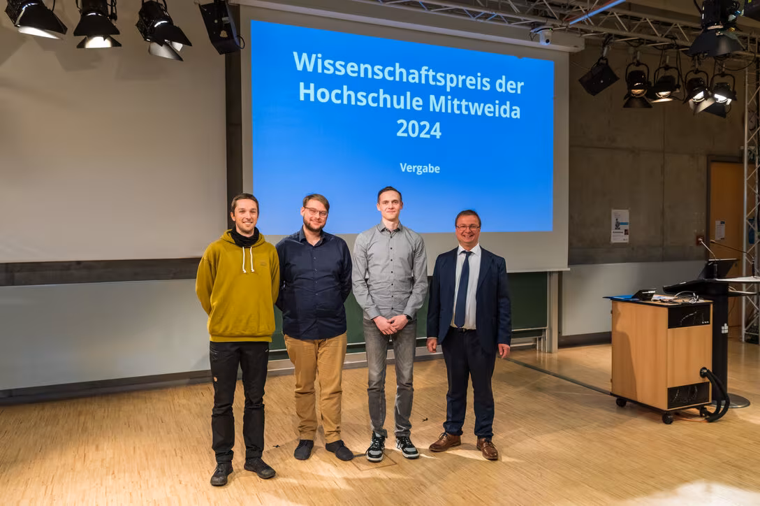 Vier männliche Personen stehen vor einer Projektionswand