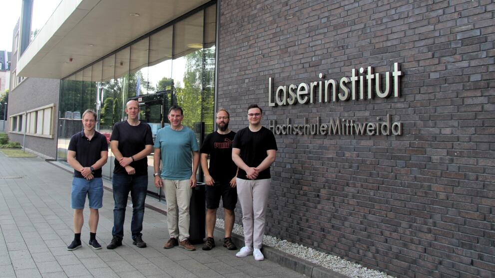 Fünf männliche Personen stehen vor einer geklinkerten Hausfront