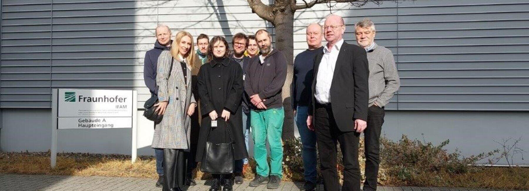 Gruppe von 10 Personen steht vor einer Hauswand und neben einem Schild des Fraunhofer IFAM