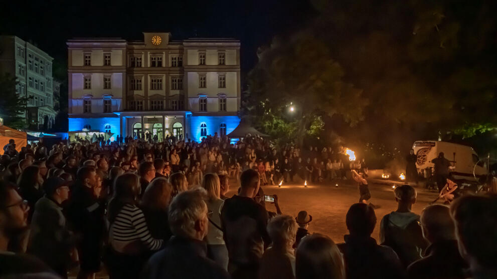 Blick auf das Hauptgbäude der Hochschule bei Naht. Im Vordergrund viele Menschen, die einer Feuershow.